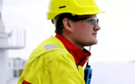 Bilde av mann med hjelm og arbeidsdress som står på båt